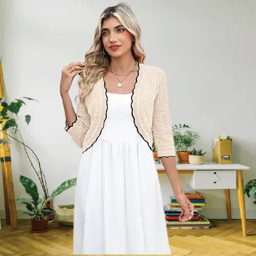 A woman wearing an elegant beige cropped knit cardigan bolero shrug over a simple white sleeveless dress.