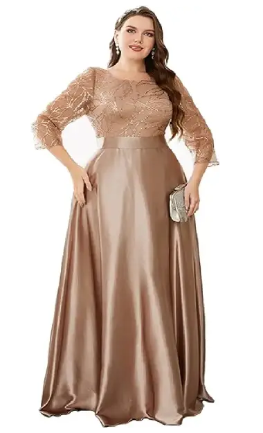 A plus-size model wearing a champagne-colored floor-length gown featuring a sequin-embellished mesh bodice, three-quarter sleeves, a round neckline, and a satin A-line skirt with a waist belt.