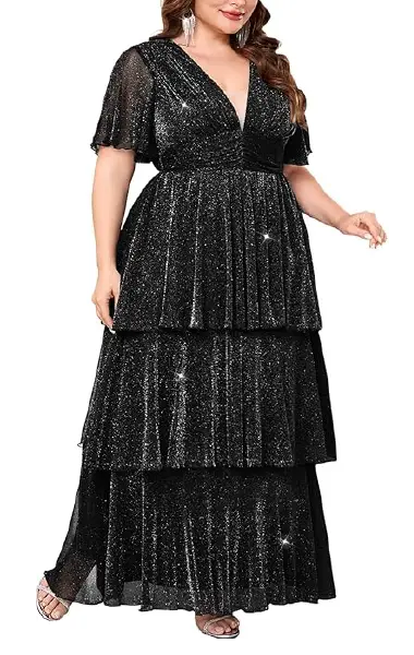 A model wearing a black, floor-length plus-size tiered maxi dress featuring a V-neckline with a nude mesh panel, flutter sleeves, and a ruched empire waist.