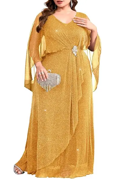 A model wearing a floor-length gold plus-size gown featuring a dual-layer design, flowy sheer cape sleeves, a V-neckline, and a ruched waist decorated with a sparkling rhinestone brooch.