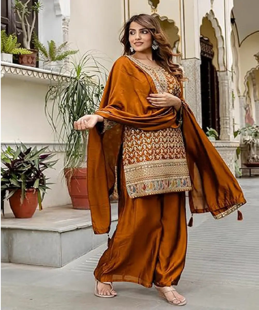 A woman modeling a mustard-colored straight kurta palazzo set made of art silk, featuring intricate sequins embroidery, a round neckline, and full sleeves.