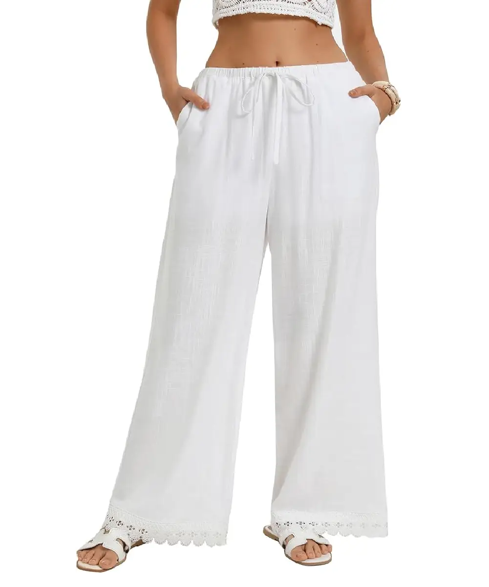 A woman wearing white wide-leg palazzo pants with a delicate lace hem, elastic drawstring waist, and side pockets, styled with white sandals.