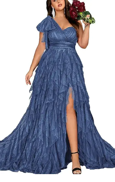 A model wearing a blue plus-size gown featuring layered mesh ruffles, an asymmetrical neckline, a decorative shoulder bow, and a high-slit skirt.