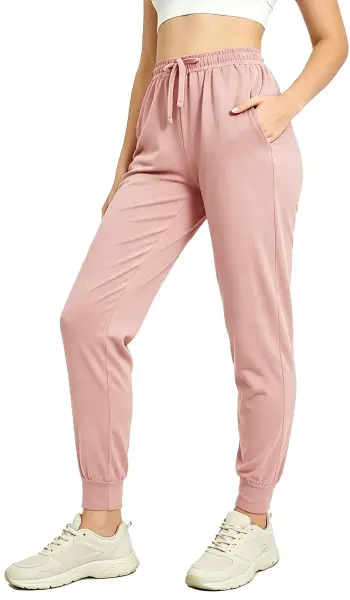 A woman modeling comfortable pink athletic jogger pants featuring an adjustable drawstring waist and cuffed ankles.