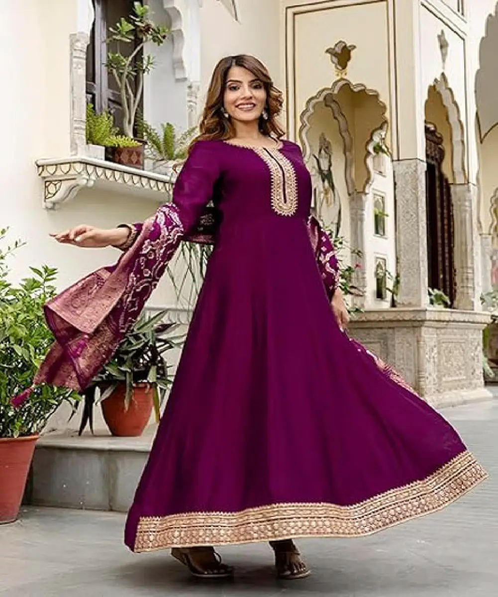 A woman wearing a purple Vichitra silk Anarkali kurta and pant set featuring intricate embroidery, a notched neckline, and a contrasting jacquard silk dupatta.