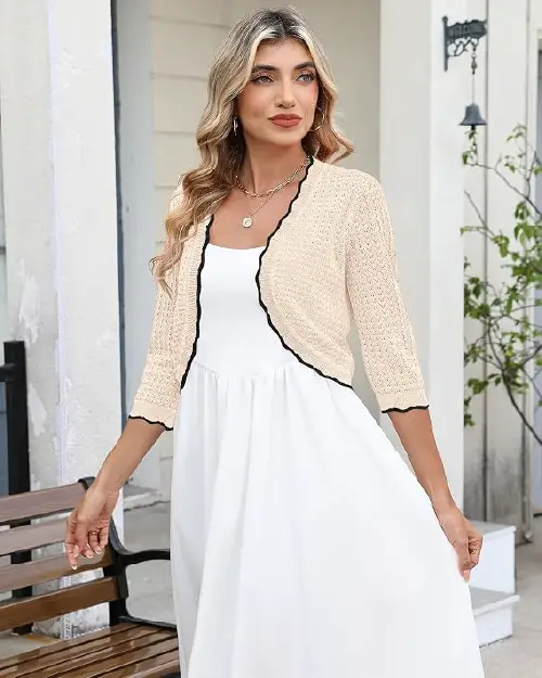 Blonde woman wearing a cream-colored open-front cropped knit cardigan over a white slip dress.