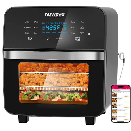 Black Nuwave digital air fryer oven with a glass viewing window showing fried chicken and vegetables inside, digital control panel, and a smartphone displaying a recipe app next to it.