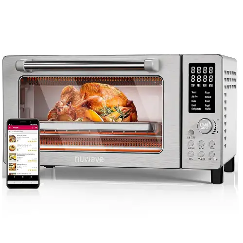 Stainless steel Nuwave digital countertop oven displaying a roasted chicken inside, accompanied by a smartphone displaying a recipe app on the left side.