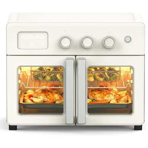 Cream-colored Martha Stewart double-door countertop oven with top control dials and digital display, showing wire baskets with Brussels sprouts and roasting trays with whole chickens inside.