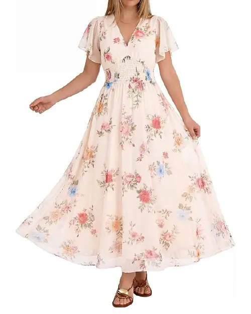 Model wearing a ivory white floral maxi dress with flutter sleeves and a wide smocked waistband, paired with slide sandals.
