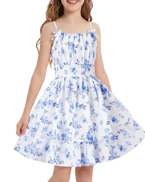 Young girl modeling a white flora dress with blue ditsy floral prints, shoulder bow ties, and a tiered ruffle skirt.