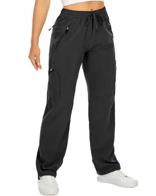 Black active cargo pants for women featuring an elastic drawstring waistband, multiple utility pockets with contrast zipper pulls, and a relaxed fit, paired with white sneakers.